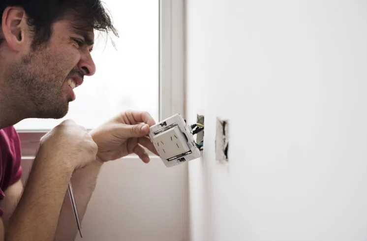 Instalação de tomadas e interruptores com fios expostos em parede residencial.